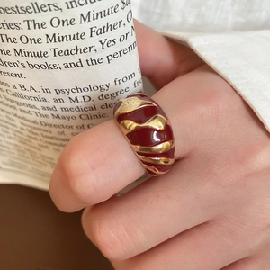 Detailed view of wide gold-plated ring with deep red enamel wave texture on finger