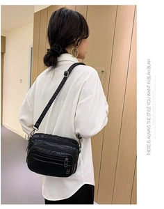 Détail du dos du sac bandoulière noir motif crocodile porté sur un mannequin en chemise blanche