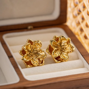 Macro detail of golden floral earrings with layered petals on a velvet jewelry box