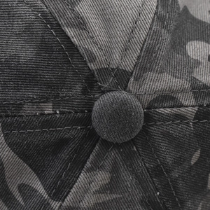 Detailed macro shot of the dark camouflage cotton twill crown and top button of the cap