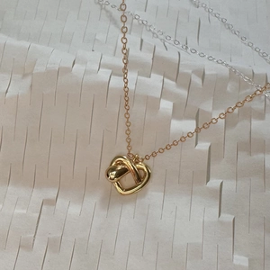 Polished gold heart knot pendant necklace with fine chain on textured background
