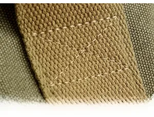 Macro shot of reinforced X-shaped cross-stitching on military green canvas bag strap