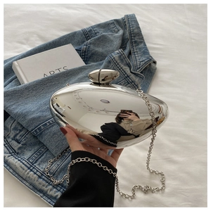 Detail of silver mirrored pebble clutch bag with metal chain on denim jacket