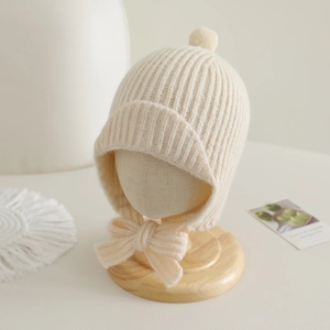 Détail macro du bonnet tricoté beige pour bébé avec pompon et nœud papillon