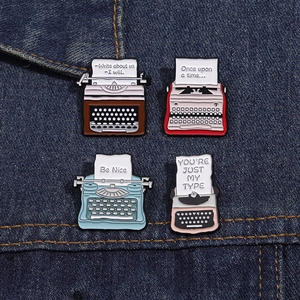 Close-up of four colorful vintage typewriter enamel pins on a dark blue denim jacket