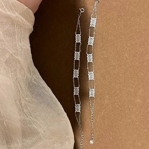 Macro detail of silver openwork floral charms and adjustable metal chain on a warm background