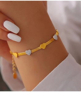 Detailed shot of golden snake chain bracelet with polished and zircon heart charms