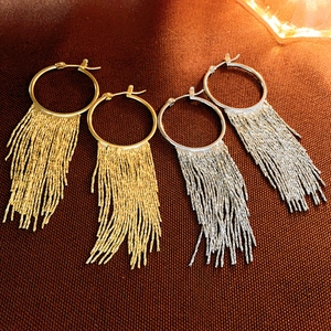 Detailed view of gold and silver metallic tassel hoop earrings on brown fabric