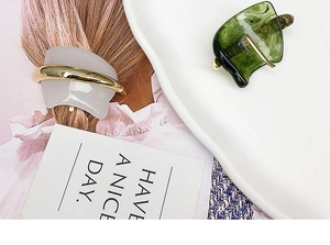 Detail showing white curved and green square resin hair clips with gold metal accents