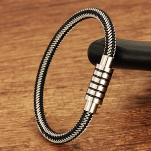 Detail of woven black and white cord bracelet with magnetic metal clasp on wood