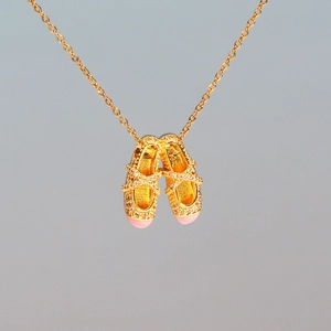 Macro shot of gold necklace featuring pink ballet slipper pendants with sparkling rhinestones