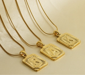 Détail de trois pendentifs carrés plaqués or 18K avec lettres R, A, K sur chaînes