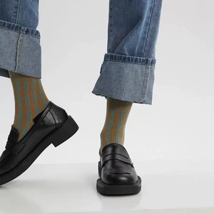 Gros plan de mocassins à plateforme en cuir verni noir portés par un mannequin en studio