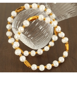 Detail of two white freshwater pearl bracelets with gold beads on dark wood background