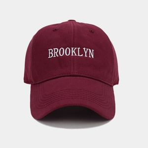 Detailed close-up of white Brooklyn embroidery on a burgundy cotton baseball cap