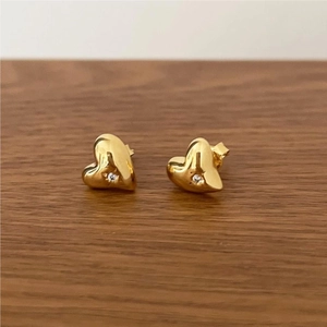 Macro shot of gold heart-shaped stud earring with a central zircon on wood background