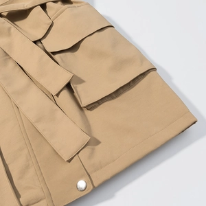 Détails de la poche du trench-coat kaki avec bouton en métal argenté et ceinture