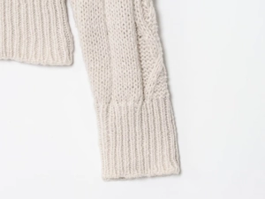 Detailed close-up of chunky knit cable texture and ribbed cuffs on oatmeal cardigan
