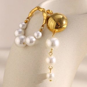 Detail of asymmetric 18K gold plated stainless steel earrings with white faux pearls