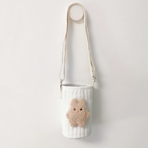 Detailed view of white quilted fabric water bottle bag with embroidered bear and shoulder strap