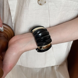 Close-up of a wide black and gold acrylic rectangle link bracelet on a wrist