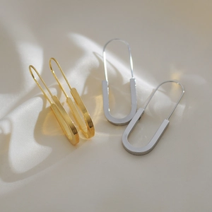 Macro shot of gold and silver U-shaped safety pin earrings on white silk fabric