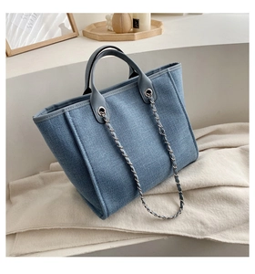 Detalle de bolso tote de lona azul con asas de cuero gris y correa de cadena de metal