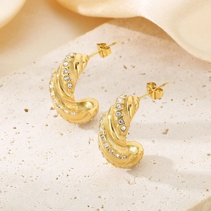 Detailed close-up of golden twisted C-shaped earrings with inlaid white zircons