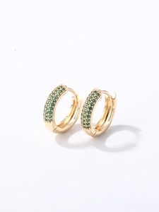 Détail de boucles d'oreilles huggie dorées avec trois rangées de zircons verts