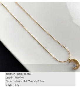 Detail view of a gold titanium steel moon pendant necklace with clear zircon stone inlay