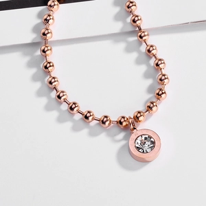 Detailed macro view of a rose gold beaded chain and Roman numeral engraved zircon charm