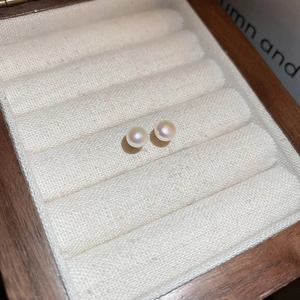 Close-up of elegant white pearl stud earrings on a soft beige velvet jewelry organizer