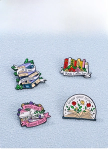 Detailed view of four enamel pins with book and floral motifs on light blue background