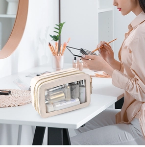 Double-layered beige toiletry bag with transparent window on a white vanity table