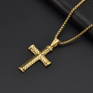 Détail du pendentif croix dorée avec texture à chevrons sur une chaîne à mailles carrées