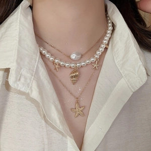 Close-up of layered necklace with starfish and shell charms worn on a female model