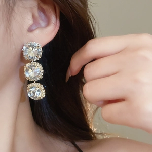 Close-up of elegant gold-tone three-tier crystal drop earrings worn by a model