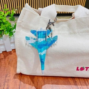 Blue camouflage fighter jet airplane pen keychain accessory on a white canvas bag