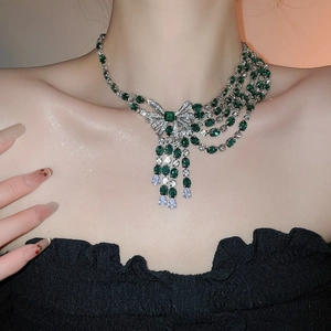 Detail of emerald and zircon bow necklace with asymmetric tassels on a model