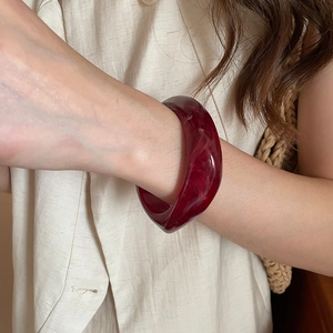 Close-up of a wide burgundy resin bangle with marble texture on a model wearing beige linen
