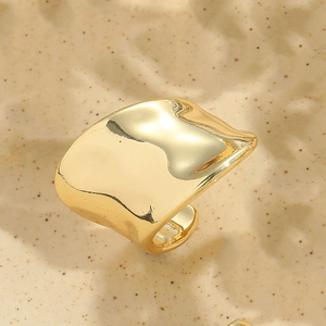 Macro shot of wide irregular gold ring showing textured metallic finish on sand