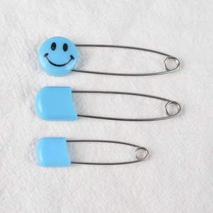 Tre spille da balia blu di varie dimensioni con motivi a faccina su sfondo in tessuto beige