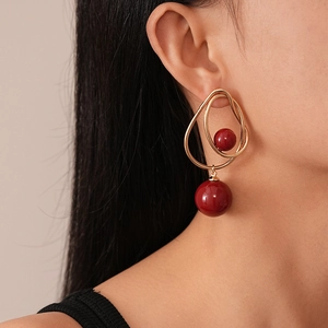 Close-up of vintage geometric gold hoop earrings with red acrylic beads on model