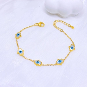Gold Hamsa Hand bracelet with blue evil eye charms on elegant white silk background
