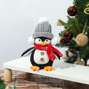 Christmas plush penguin toy with gray knit hat and red striped scarf on a white stand