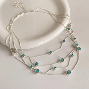 Detail of silver multi-layer necklace with blue round gemstones on a white ceramic plate