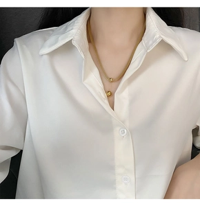 Dettaglio di una collana dorata con doppia perla indossata da una modella in camicia