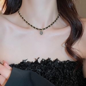 Close-up of gold-plated woven leather chain necklace with black camellia pendant on a model