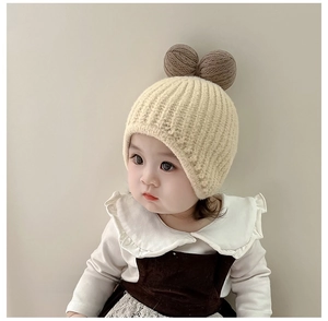 Detail view of baby beige knit hat with brown pom-pom ears and soft texture