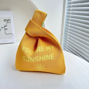 Detail of knitted tote bag with Sunshine text and knot handle on a white desk